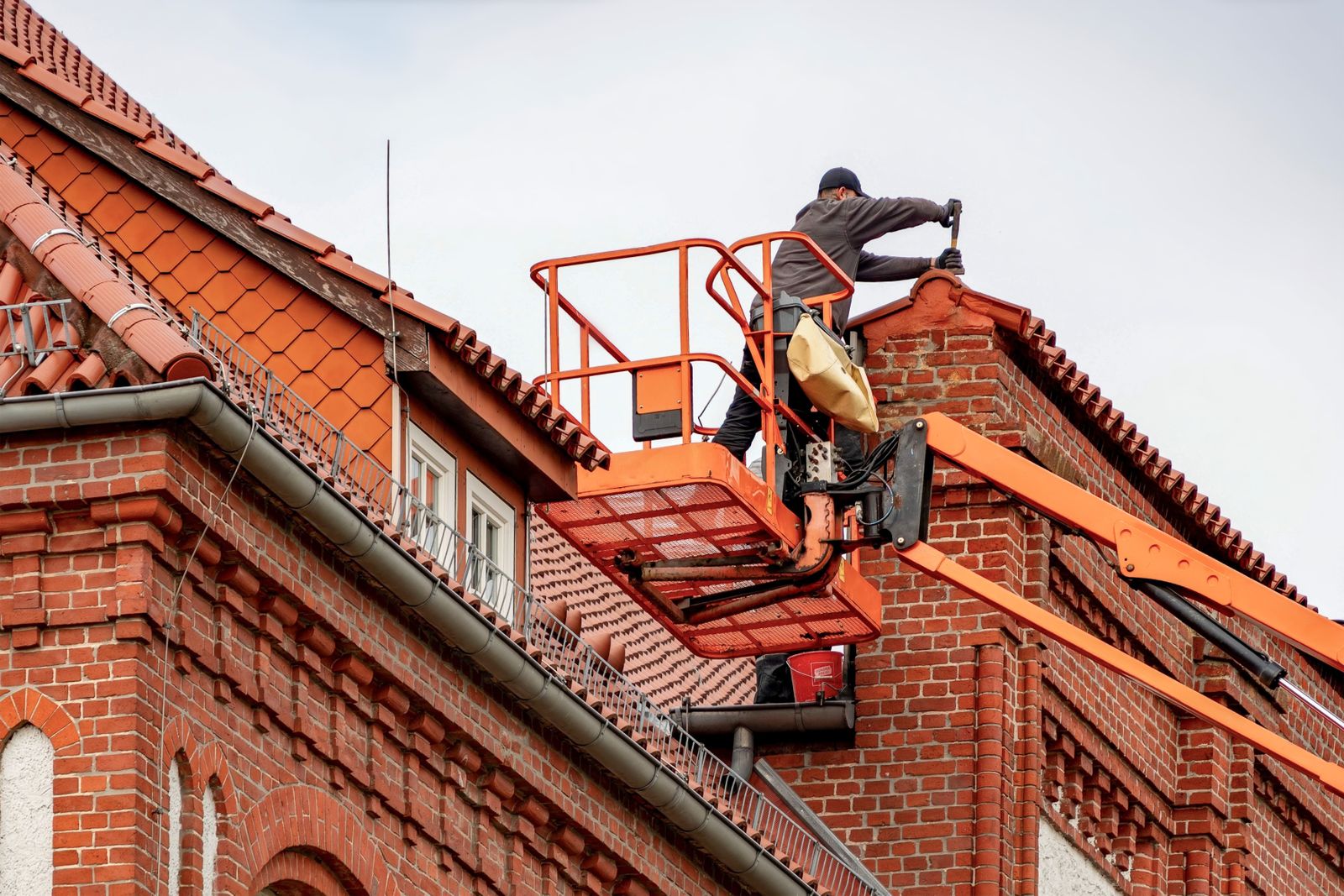 Gutter Repair in Piscataway NJ — Roofer in a cherry picker conducting maintenance on a red brick building with a tiled roof.