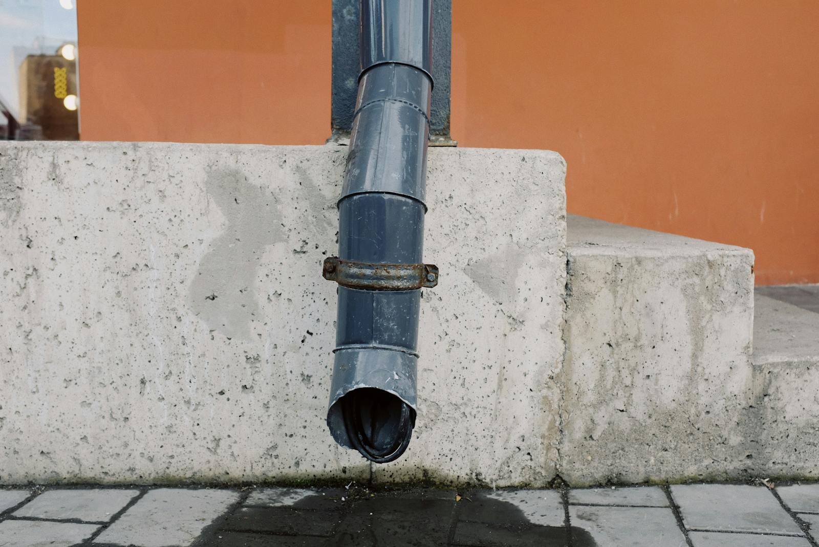 Downspout Cleaning in Piscataway NJ — Aged metal drain pipe on a concrete wall with water stains, highlighting urban decay.